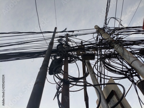 фотографія Chaotic tangle of telephone and electrical wires on poles against cloudy sky