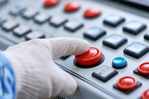 Close-up of a gloved hand pressing a red button on an industrial control panel with multiple buttons.