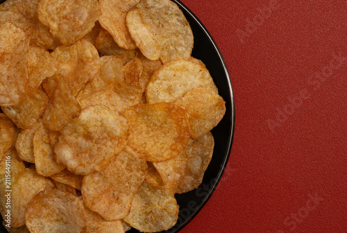 Close up spicy potato chips tasty snack Chili-spiced appetizer on a black plate red background, flat-lay view image suitable for menus parties marketing.