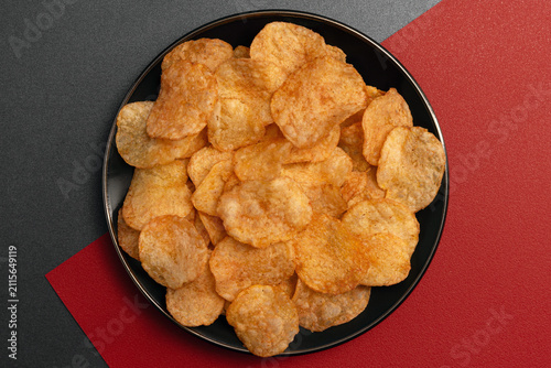 Spicy potato chips tasty snack Chili-spiced appetizer on a black plate red background, flat-lay view image suitable for menus parties marketing.