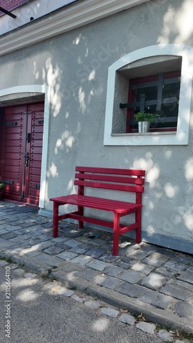Red park benches outside a building with cobblestone pathway and dappled sunlight