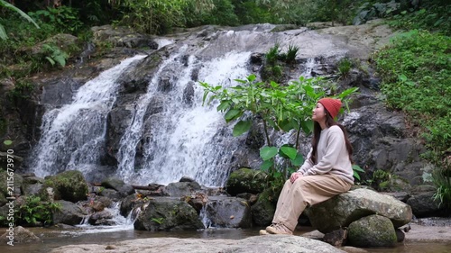 A woman traveller sitting by the waterfall in the forest