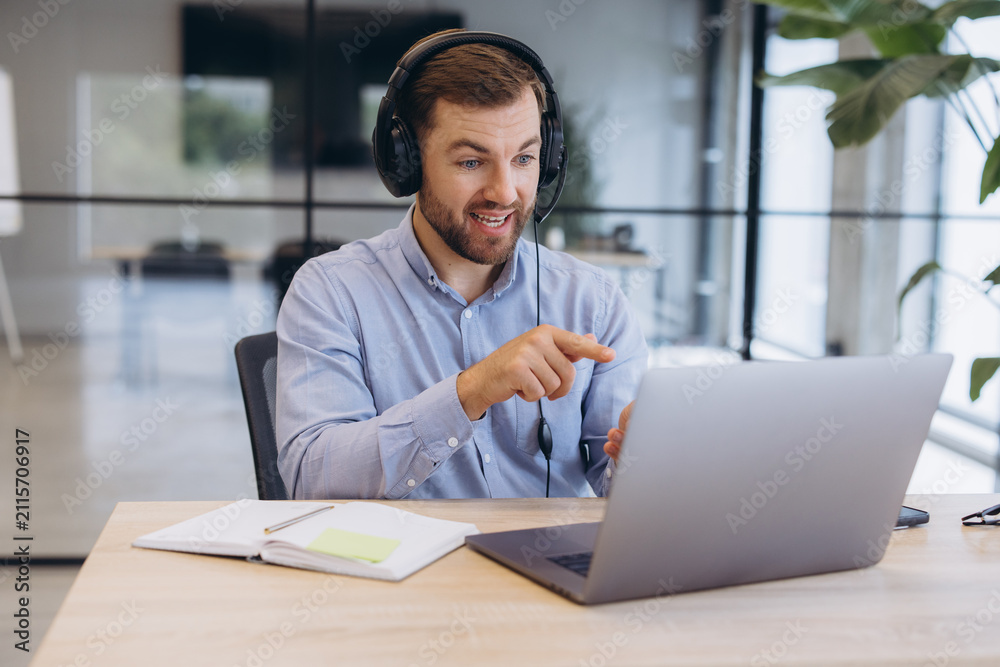Fototapeta premium Businessman wearing a headset participating in a video call, discussing and pointing at his laptop screen