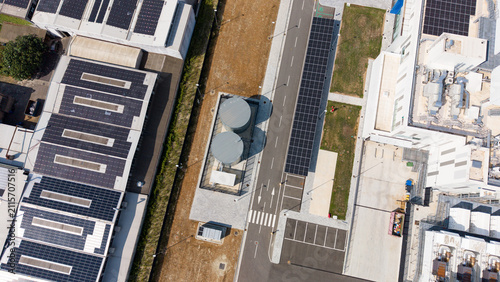 Aerial view of a modern data center campus with solar panels on rooftops, large storage tanks, and paved access roads in Melegnano, Lombardy, Italy.
