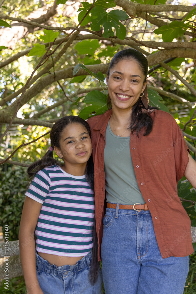 Obraz premium African American mother and youth daughter smiling under leafy canopy in garden, wearing belt
