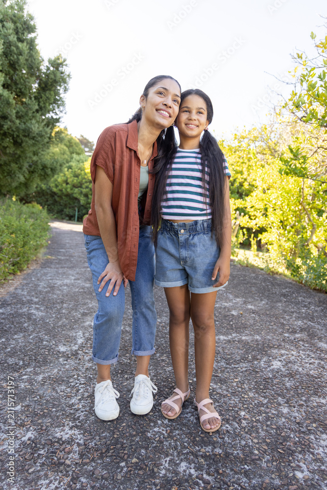 Obraz premium Mother and daughter standing on paved park path, wearing rust shirt and striped t-shirt