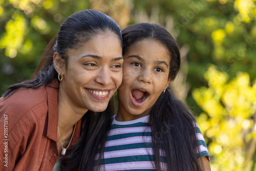 African American mother and youth daughter leaning, smiling in park with pendant, striped shirt