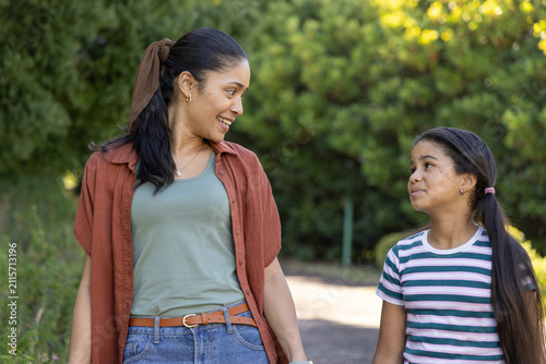 African American mother and child walking and talking on paved park path, wearing rust overshirt