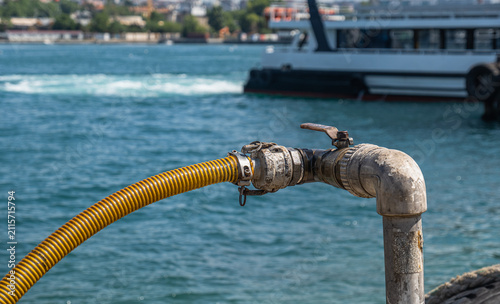 A large water valve and plastic hose by the sea.