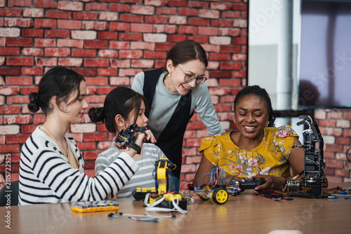 Robotics Education with diverse female teachers and Asian students smiling while exploring robotic hands, electronic equipment, and STEM projects together