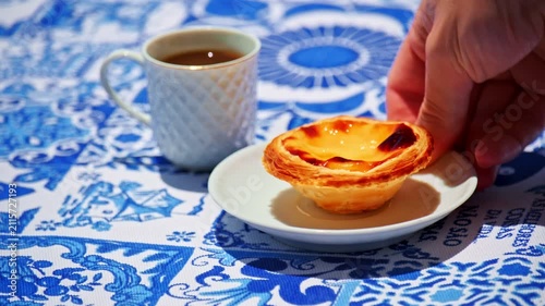 A hand placing white plate with a pastel de nata beside a coffee cup