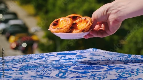 Hand placing three pastel de nata tarts and glass of meia de leite