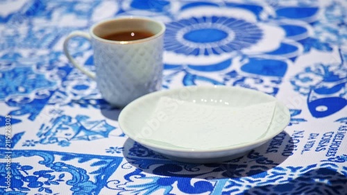 Hand placing and lifting a pastel de nata beside a coffee cup on blue