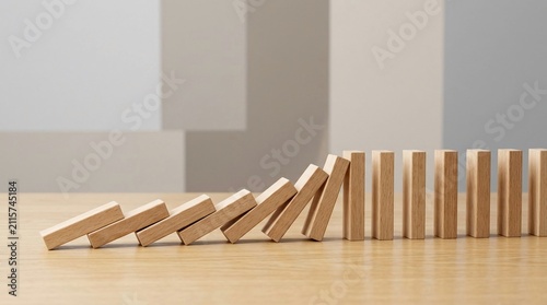 Chain reaction of wooden domino blocks falling on a light wood surface against a neutral minimalist background, illustrating cause and effect and sequence of events in a row.