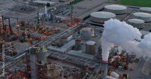 Aerial view of Joliet oil refinery with industrial pipes, storage tanks, and smoke rising from a chimney at sunset in Joliet, Illinois, United States.