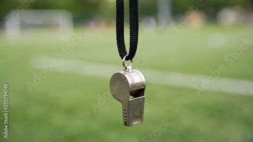 Silver metal referee whistle hanging from a black lanyard on a blurred green sports field background