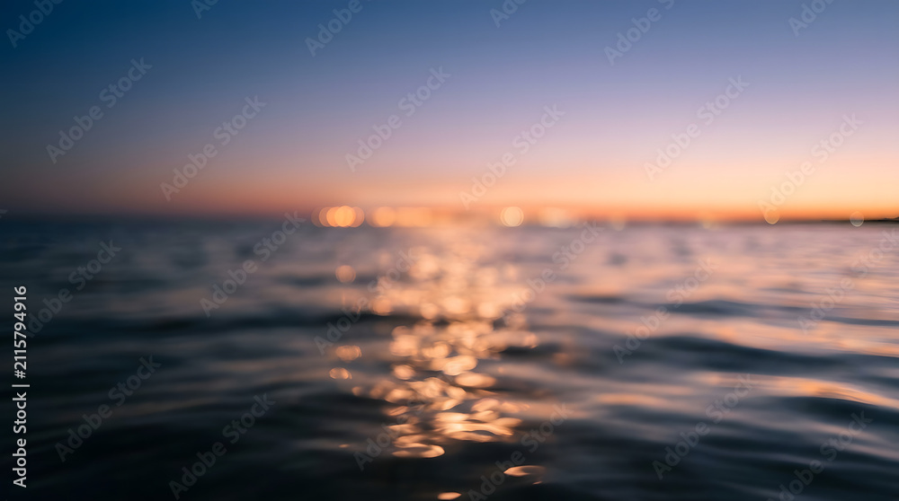 Fototapeta premium Sunset over calm ocean with golden reflections. Serene seascape featuring soft horizon glow and tranquil water surface.