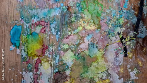 Photography Horizontal close-up of a wooden tabletop covered in abstract acrylic paint splatters, smudges, and drips