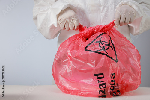 Bild auf Leinwand Cautious health worker wearing protective glove seals red biohazard waste storag