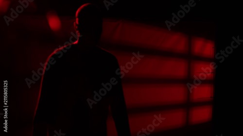 Mysterious man emerging from dark red-lit background and pressing open palm toward camera lens in dramatic close-up. Cinematic thriller concept for security, crime, mystery and dramatic storytelling a