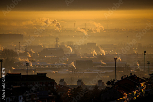 Aerial view of heavy smog and industrial smoke rising over the urban skyline of Turin during a golden sunset in Turin, Piedmont, Italy.