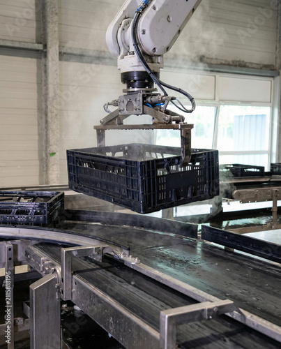 Industrial Robotic Arm Lifting a Plastic Crate from a Conveyor
