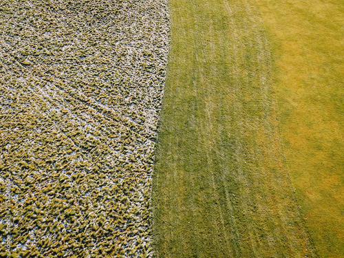 Aerial view of a golf course showing a distinct contrast between a frost-covered textured section and a vibrant green grassy area in Valmiera, Valmiera, Latvija.