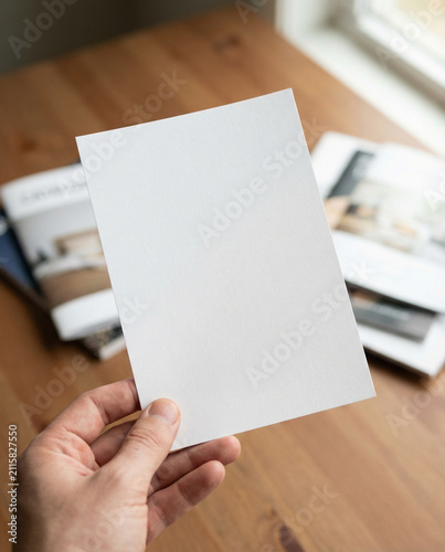 Hand Holding a Blank Vertical Card with Magazines in the Background