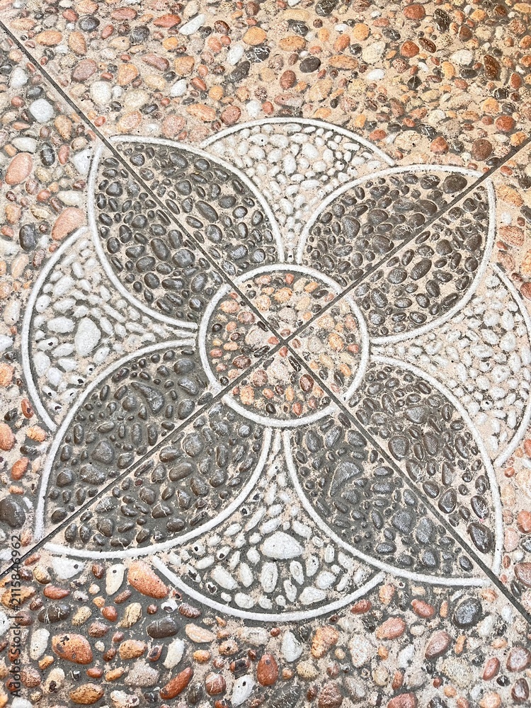 Obraz premium Top-down view of square stone tiles featuring an intricate, geometric medallion or floral pattern made of multi-colored pebbles, dark gray stones, and white gravel set in concrete.