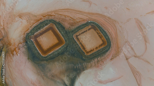 Aerial view of Koyuncu Salt Works, showing two distinct square salt evaporation ponds with reddish-brown water surrounded by textured salt flats in Sereflikochisar, Ankara, Turkiye.