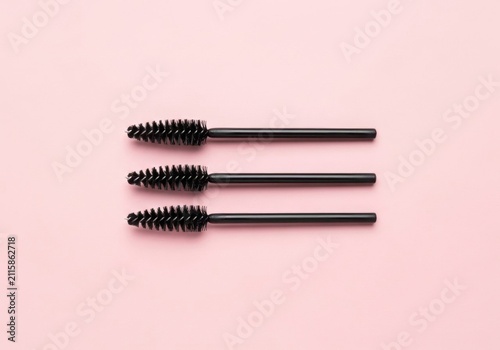 Three black mascara wands on a pink background