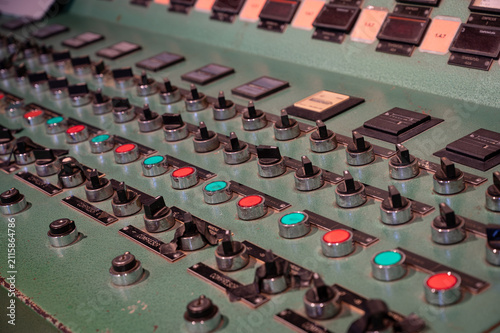 Detailed view of a vintage complex industrial control panel featuring rows of rotary switches, knobs, and colored push buttons.