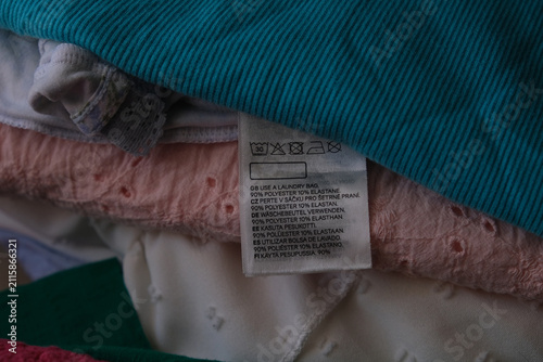 Obraz na plátně Close up of a clothing care label on a stack of colorful folded garments showing washing instructions