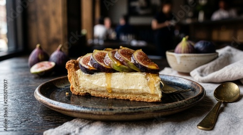 Slice of vanilla custard tart topped with fresh sliced figs and honey drizzle on a dark ceramic plate in a cozy cafe setting