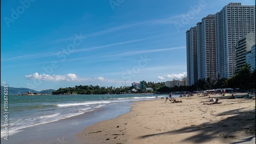 Sunny day at Nha Trang Beach, Vietnam, featuring a sandy shoreline, calm sea, modern high-rise buildings and distant mountains along the tropical coastline.
