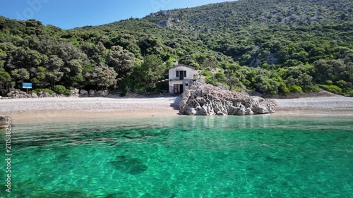 Crystal-clear Adriatic waters embrace the peaceful coastline of Sveti Ivan Beach on Cres Island, Croatia, where emerald-covered slopes descend toward a pebble cove dotted with anchored sailing boats.