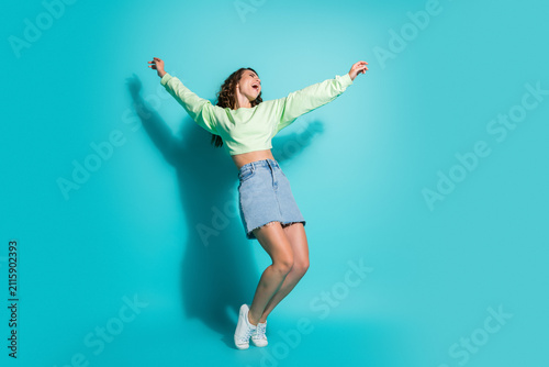 Fotografía Happy young woman jumping in casual denim skirt and sneakers on a vibrant turquo