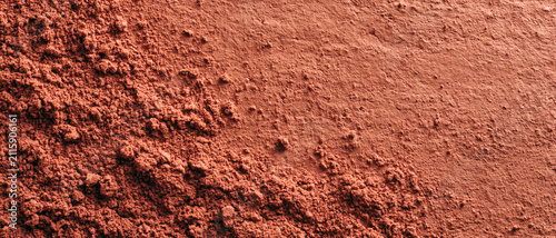 A pile of red clay powder covers a flat surface creating a textured background that shows natural earth pigment materials used for artistic and cosmetic purposes