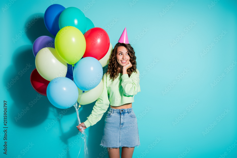 Obraz premium Young woman holding colorful balloons and wearing a party hat celebrating a birthday in a bright turquoise studio portrait