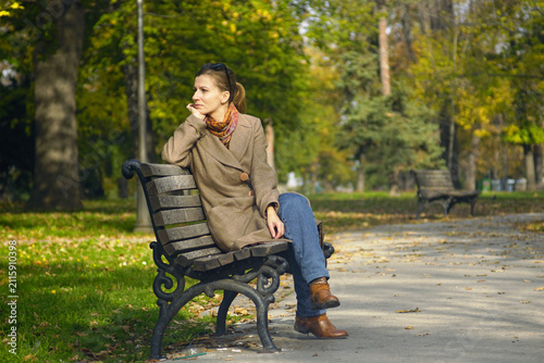 Foto Woman resting on wooden park bench beside tree-lined pathway in autumn