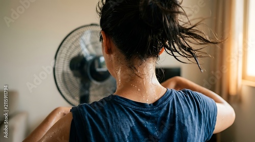 Overheated woman cooling down with electric fan during intense summer heat wave at home with standing front electric messy hair standing