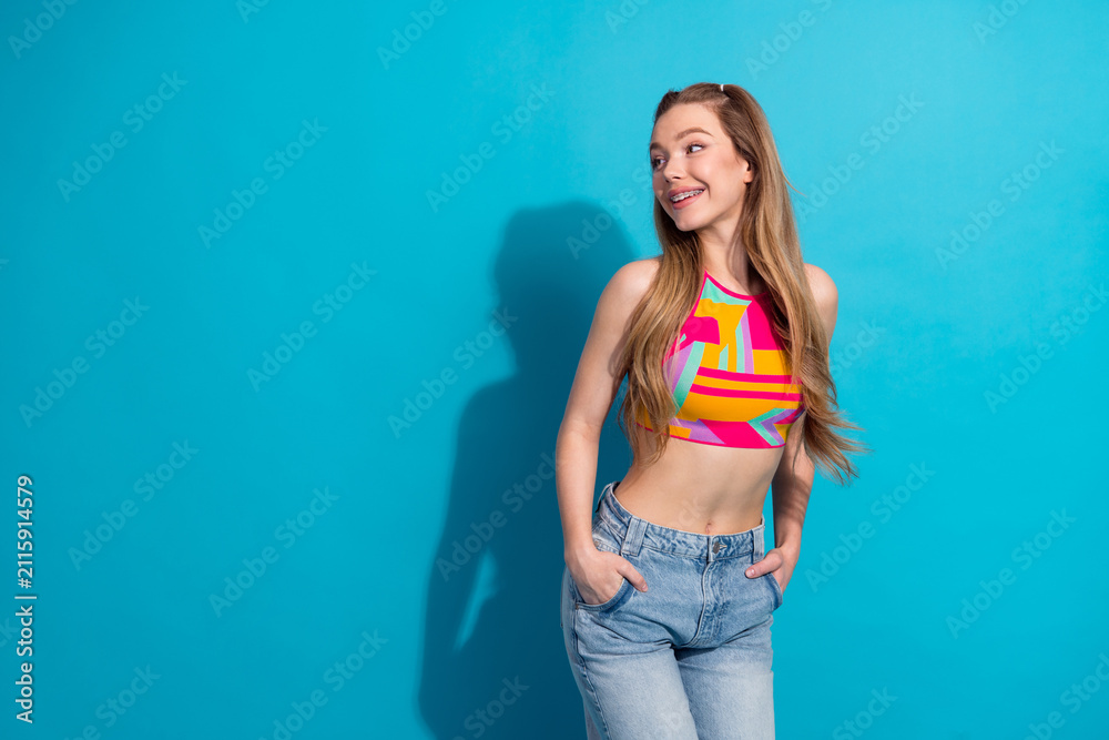 Obraz premium Lifestyle portrait of a young woman in colorful top against blue backdrop exuding happiness and stylish charm