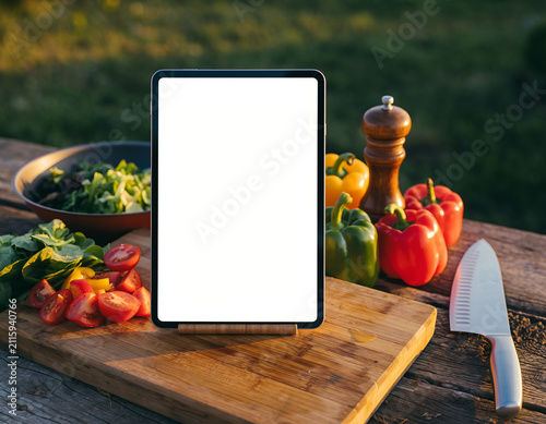 Cooking tablet stands on a wooden kitchen counter with fresh ingredients around it