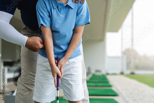 Golf Coach correcting an Asian boy's upper body position and grip during a close-up junior golf lesson at a covered driving range practice area