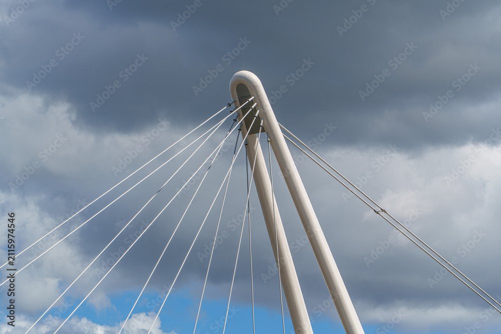 Fototapeta premium Modern architectural cable-stayed bridge pylon standing tall against a dramatic cloudy sky symbolizing engineering progress.
