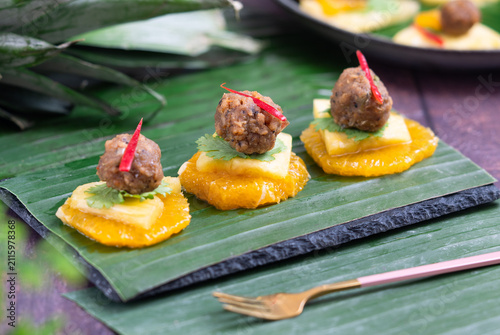 Traditional Thai royal appetizer Ma Hor featuring savory minced pork ball over fresh orange and pineapple slices served on banana leaf.