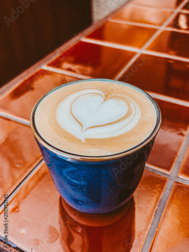 Cup of cappuccino with heart shaped latte art on a colorful tiled table