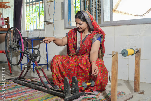 Indian woman wearing using a traditional charkha spinning wheel, transforming raw cotton into fine thread for weaving handmade textiles. Skill india and women empowerment.