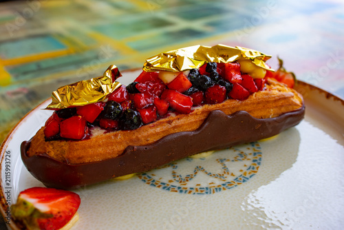 Obraz na płótnie Gourmet eclair topped with fresh berries and gold leaf on plate
