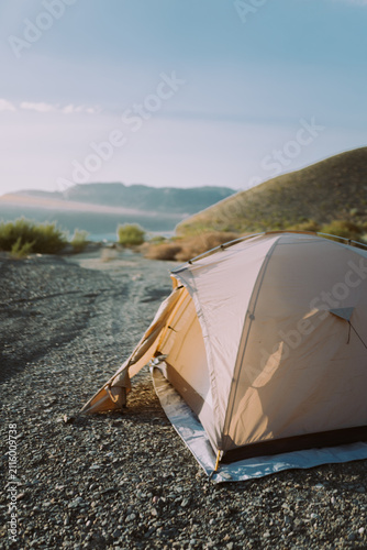 Tourist tent pitched on river bank with mountains in background, camping adventure